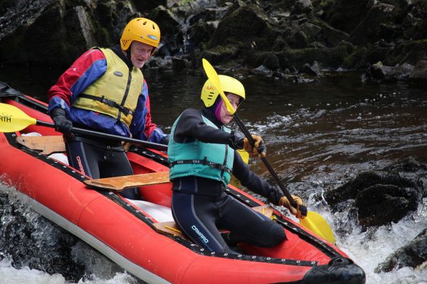 Rowers navigating rapids near rocks