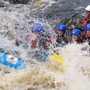 Outdoor instructor training course - People wearing safety helmets and life vests taking part in a white-water rafting activity.