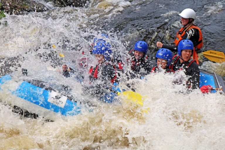 Outdoor instructor training course - People wearing safety helmets and life vests taking part in a white-water rafting activity.