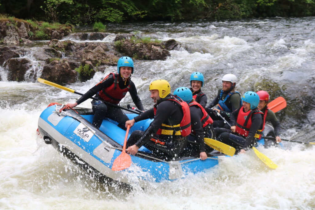 A group of people wearing safety gear, enjoying an Active Outdoor Pursuits white water rafting adventure