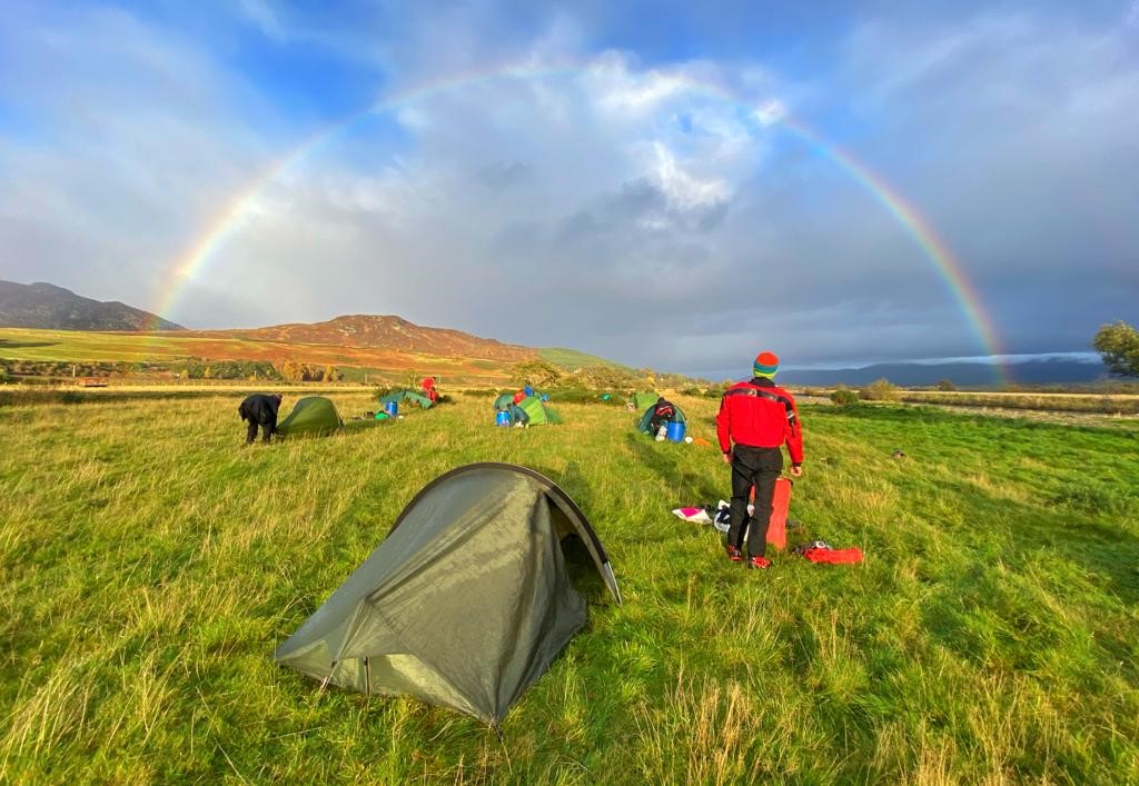 A group of Duke of Edinburgh participants camping with a rainbow in the background